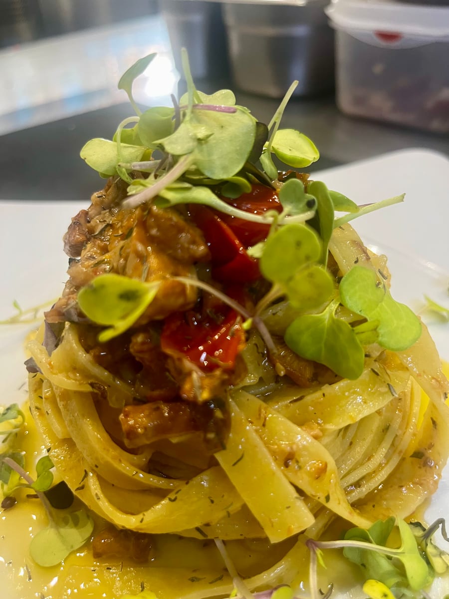 Tagliatelle con finferli freschi, pomodorini confit e germogli. Primo piano stretto, nitidissima, verticale ad alta risoluzione. Scattata al passe: su